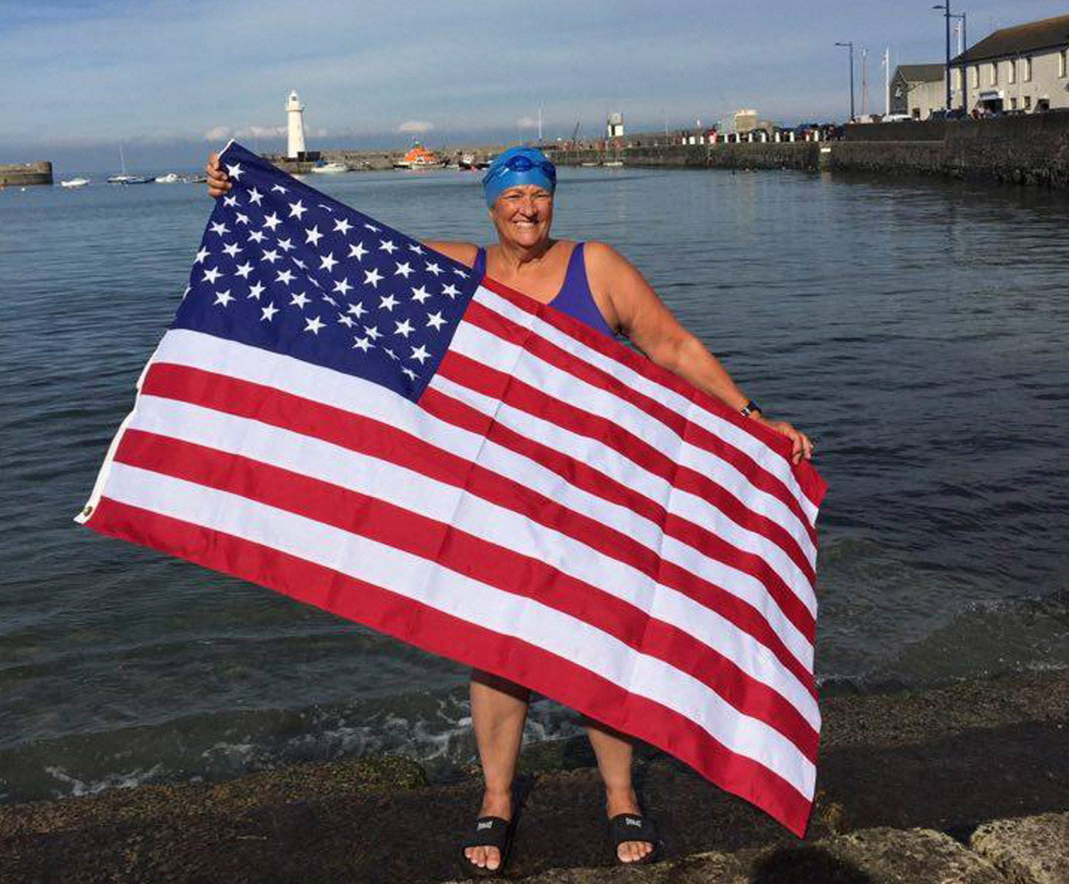Pat Gallant-Charette holds an American flag on the shore of Donaghadee, Northern Ireland, Thursday to celebrate her crossing of the North Channel of the Irish Sea the previous day. She left from Donaghadee and swam to Scotland. Photo by Tom Charette