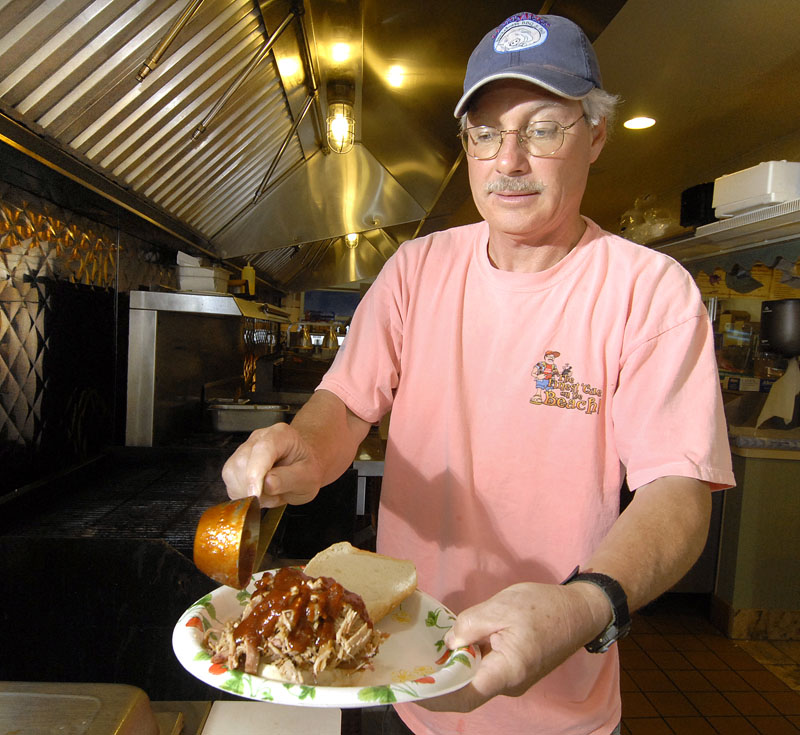 In this 2007 file photo, Dennis Sherman, owner of DennyMike's smokehouse in Old Orchard Beach, adds some of his special BBQ sauce to a Texas-style pulled pork sandwich.