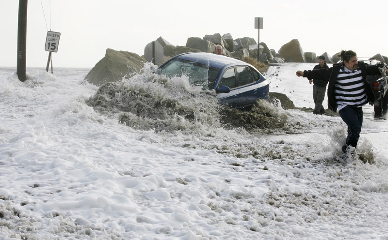 a wave breaks over an occupied car as people attempt to tow it to safety Friday at Camp Ellis in Saco. The driver left the car as the tide rose and flooded local streets.
