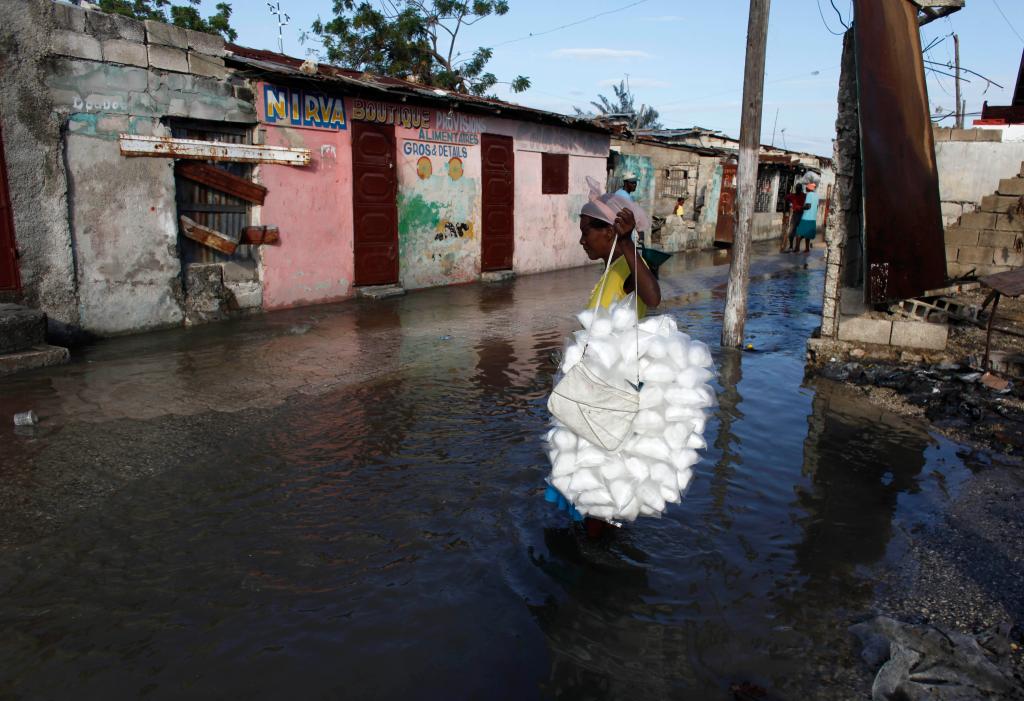 A woman carries cotton candy through a flooded street caused by heavy rains overnight in the Cite Soleil neighborhood of Port-au-Prince, Thursday Feb. 18, 2010. The capital city of Haiti is particularly vulnerable to rains at this moment as it recovers from the heavy damage it suffered during last month's earthquake. (AP Photo/Javier Galeano)
