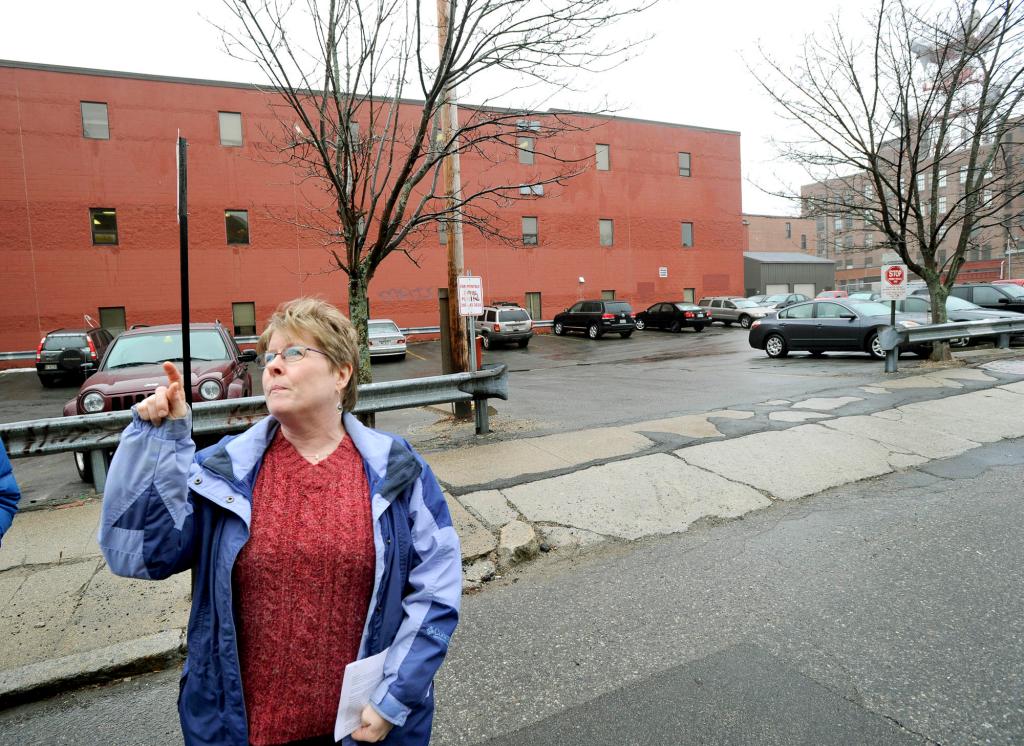 Susan Fitzpatrick points to her condo building while standing in front of an Oak Street parking lot where affordable housing is planned. Fitzpatrick opposes the project because “I don’t want my property’s value driven down.”