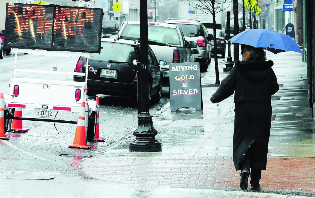 Staff photo by Joe Phelan A woman walks past a flood watch sign at the corner of Winthrop and Water Streets in downtown Augusta on a cold, rainy and windy Wednesday afternoon. A flood watch is in effect through Friday and the National Weather Service forecast calls for a rain snow mix.