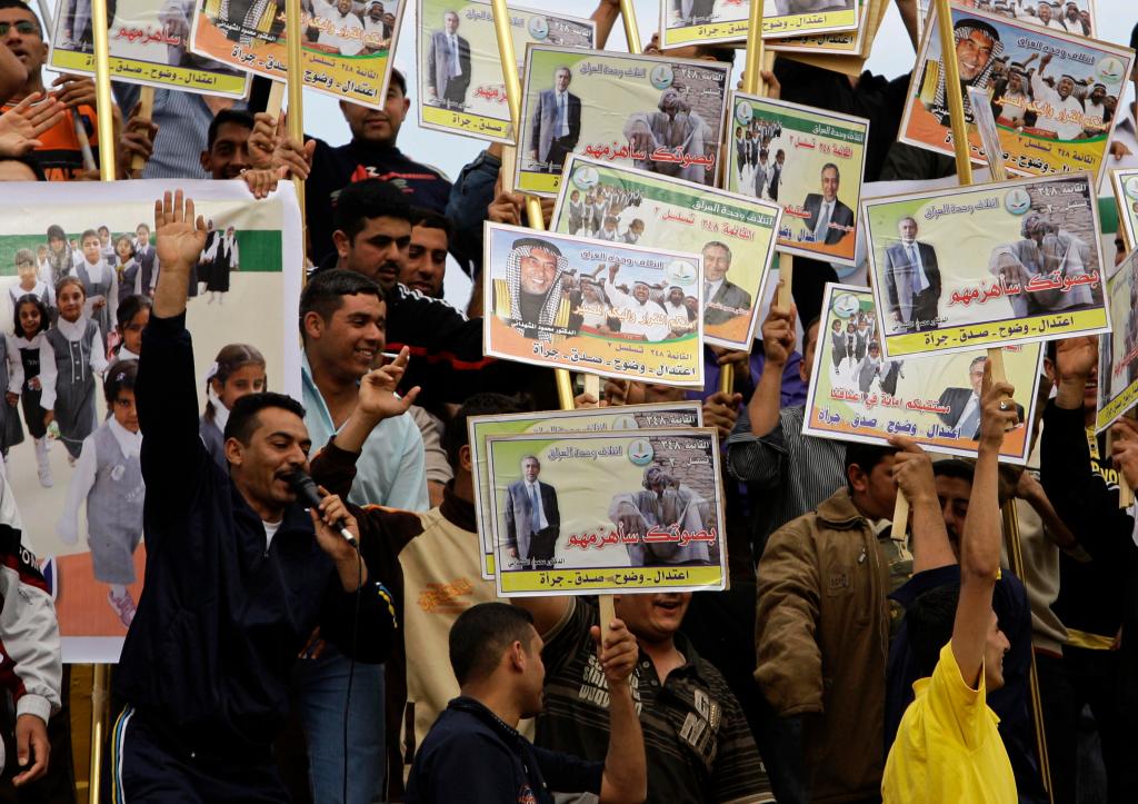 Men hold campaign posters of Mahmoud al-Mashhadani, a candidate with the Iraq Unity Alliance, at a rally in Baghdad on Saturday. Parliamentary elections are March 7.