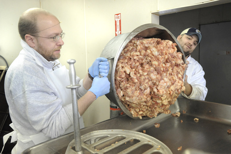 Reporter Ray Routhier, left, helps Marc Mailhot pour a container of pork into the grinding machine while learning the sausage business at Mailhot’s Best, in Lewiston.