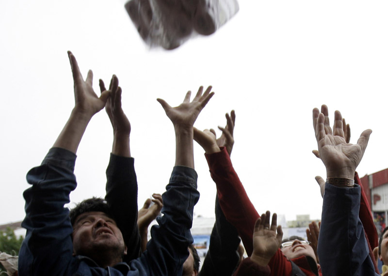 People reach for goods thrown from a supermarket window in Concepcion, Chile, today. Security forces said they arrested dozens of people for violating an anti-looting curfew.