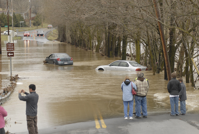 People stare at two abandoned vehicles that bogged down while the drivers were trying to cross Golf Course Road in Martinsburg, W.Va., Sunday. The Opequon Creek overflowed its banks Saturday, causing local officials to close several low-lying roads. In the Northeast, thousands lost power in Pennsylvania, New Jersey, New York and Connecticut. Flood