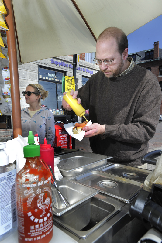 Ray Routhier tries to get the squiggle of mustard to look just so as he works the hot dog stand of Jess Cady-Giguere in Portland.