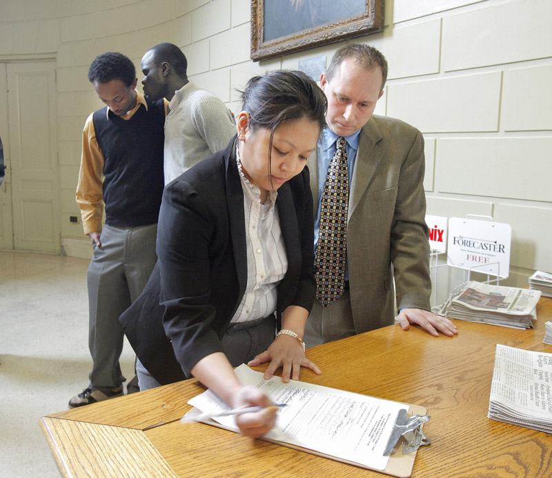 Will Everitt watches as Jenna Vendil signs an affidavit today to initiate a petition drive looking to give non-citizens the right to vote in city elections. In the background are two other members of the committee initiating the petition, Mohammed Dini, left, and Alfred Jacob. The group needs to gather 4,500 signatures to put the referendum on the November ballot.