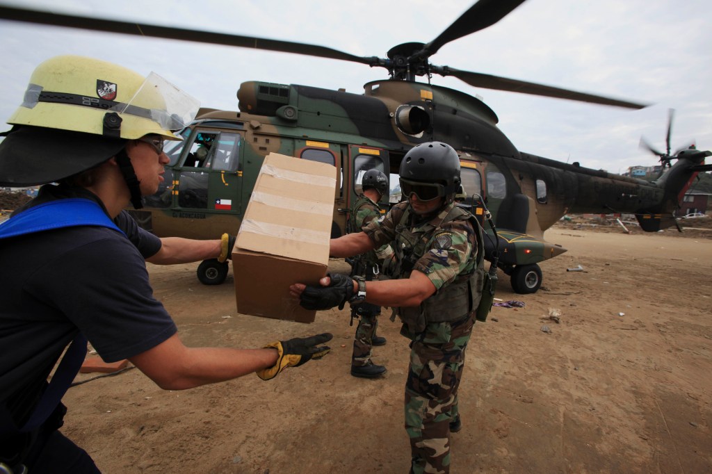 Troops and firefighters unload relief supplies from a military helicopter Wednesday in Dichato, Chile. The government deployed thousands of troops throughout the country's central coastal region to curb looting and facilitate aid distribution.