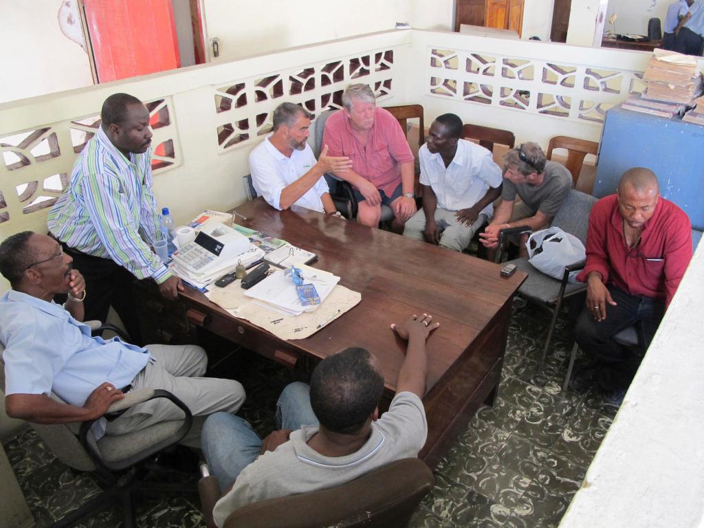 Haitian officials wait while Hope Village founder Father Marc Boisvert, Sea Hunter owner Greg Brooks, interpreter Felix Vital and ship Captain Gary Esper confer Wednesday during discussions on offloading the Maine relief ship's cargo in Les Cayes.