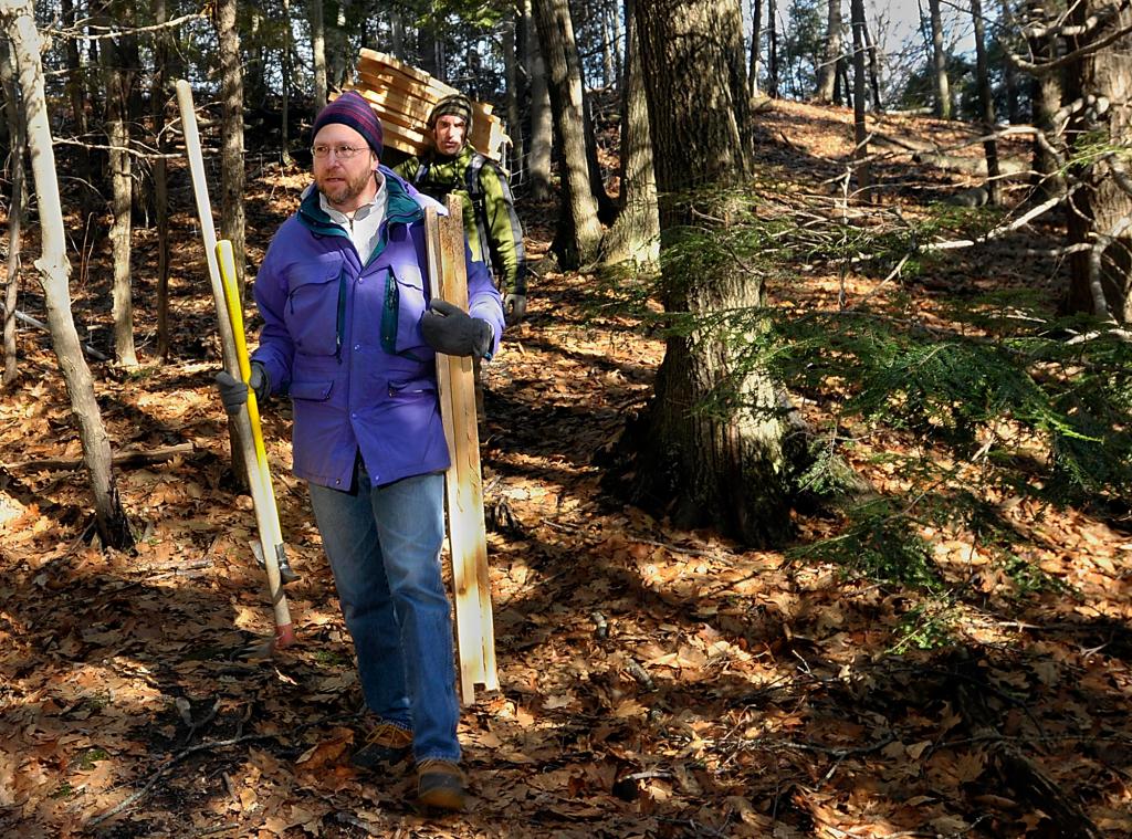 Ray Routhier carries tools and wood to help build a new bridge at the Fore River Sanctuary in Portland. Behind him is Jaime Parker, trails manager.