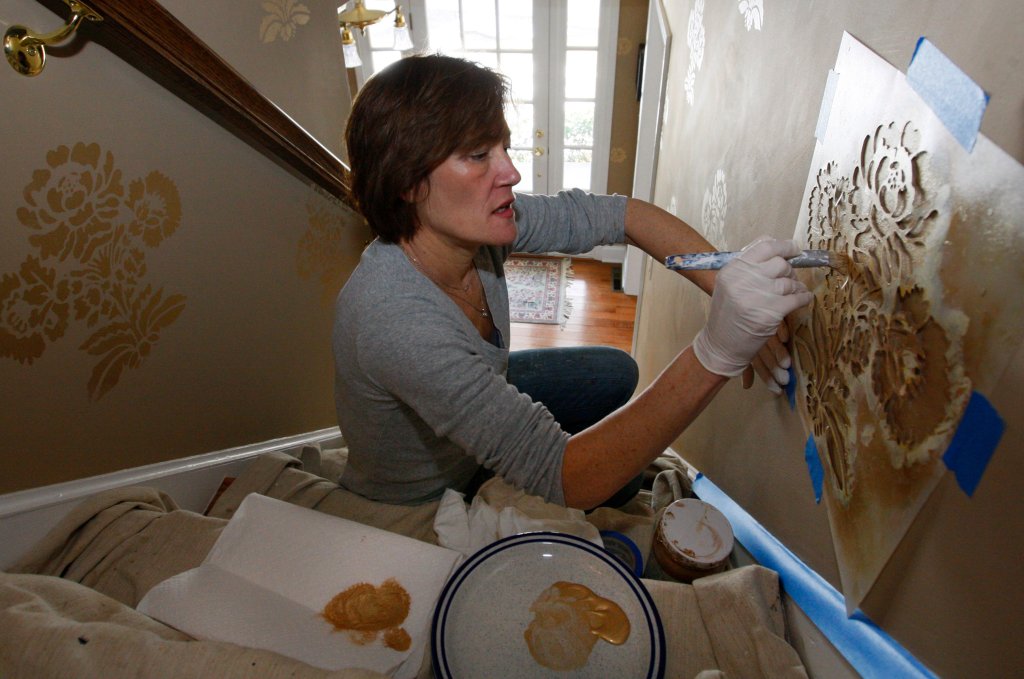 Decorative painter Tracy McGranaghan works on a stairway stenciling project. The process can make “a plain door look like cherry or a plain plaster column look like marble,” she said.