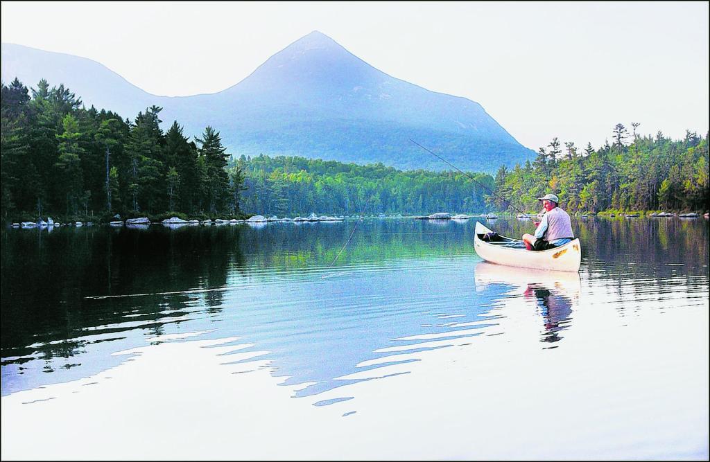 A fisherman tries his luck on Rocky Pond, with Doubletop Mountain in the background and reflected in the water. In the northern half of Maine, the fishing season will remain the same in order to protect the prized native brook trout fisheries there.
