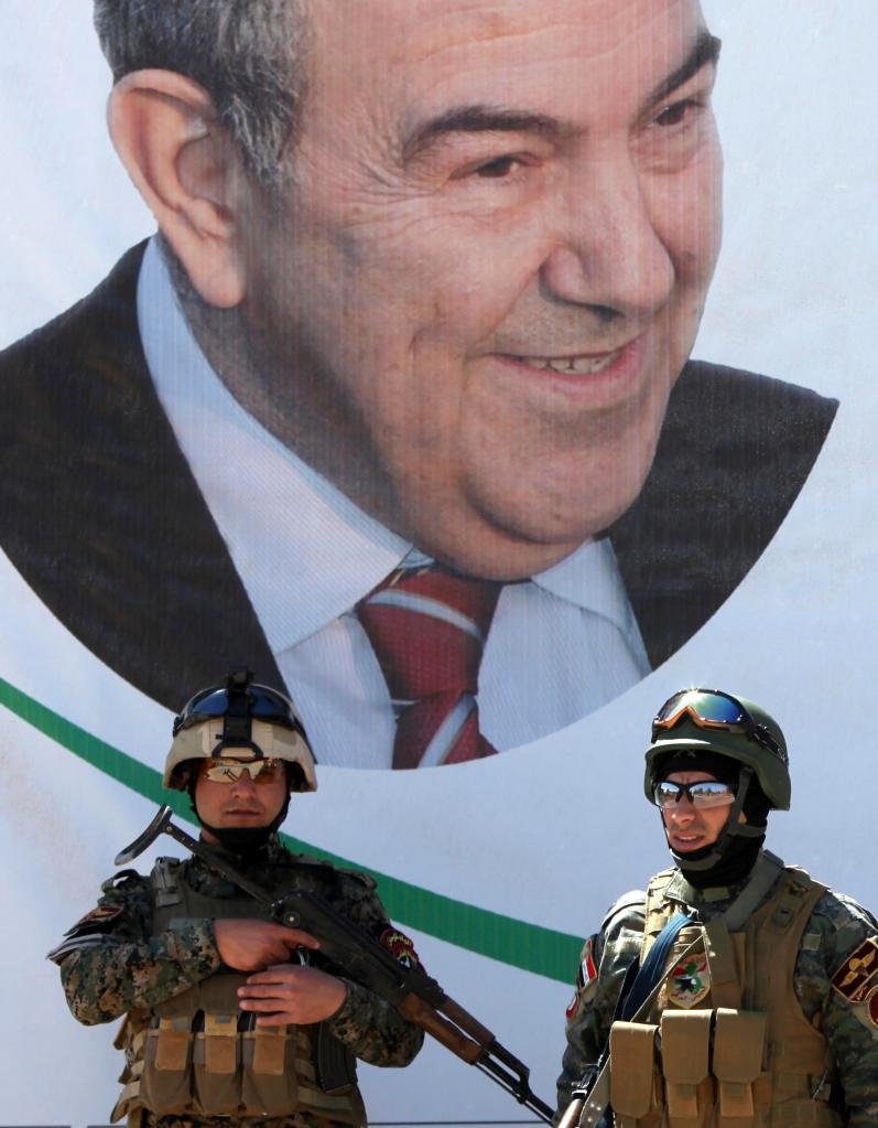 Iraqi policemen stand guard in front of an election campaign poster for former Iraqi Prime Minister Ayad Allawi at a checkpoint in Baghdad, Iraq, on Saturday.