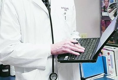 Dr. Joe Davison uses a computer tablet to access patient information at West Wichita Family Physicians in Wichita, Kan. Health care providers can recoup some of the costs of such systems.
