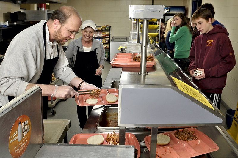 As hungry students pass through the lunch line, reporter Ray Routhier makes pulled pork sandwiches at the Cape Elizabeth Middle School cafeteria under the guidance of Judy Levesque. Levesque and the students showed patience.