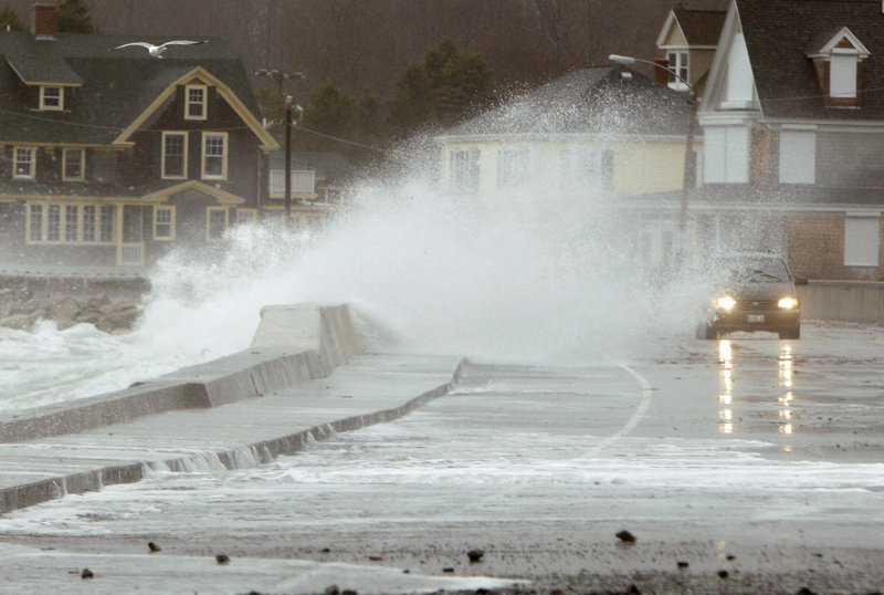 A wave crashes over a sea wall as a car makes its way along Beach Avenue in Kennebunk on Monday.