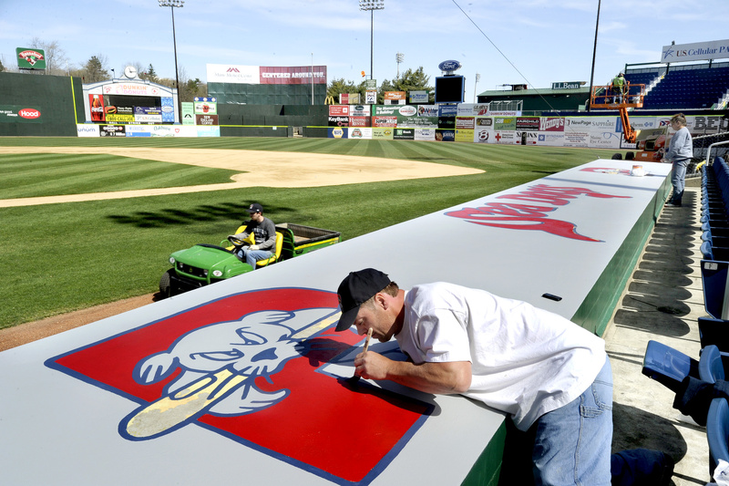 Sun-drenched Hadlock Field buzzes with activity Tuesday as workers get the field, dugouts and stands ready for the Portland Sea Dogs home opener Thursday. Painting the team logo on top of the home dugout are Mike Daigle, left, and Anthena Court.