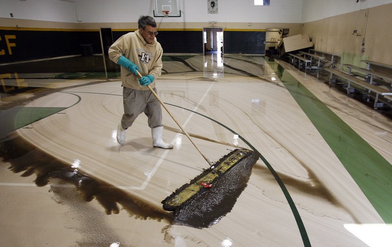Ron Chopoorian, a volunteer at Cranston League for Cranston’s Future, a boys and girls youth organization, sweeps water out of the gymnasium Friday after flooding from the Pawtuxet River left the gym under 4 feet of water.