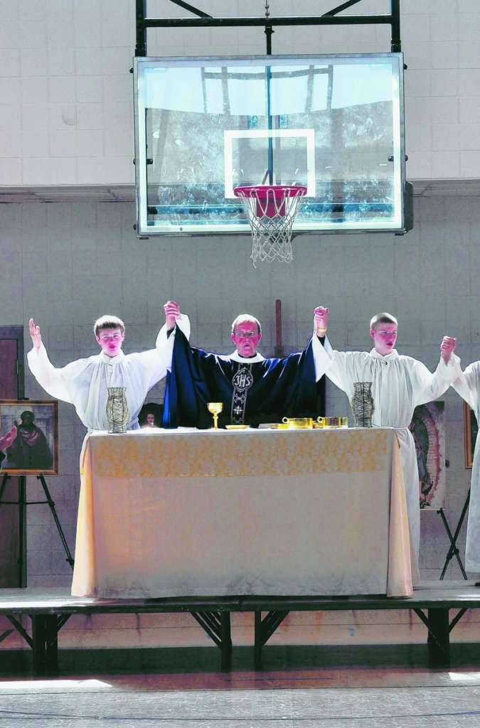 St. Matthew’s Monsignor John McSweeney, center, leads Sunday Mass in the parish center gym in Charlotte, N.C. “Catholic services do not function without a priest present,” he notes.