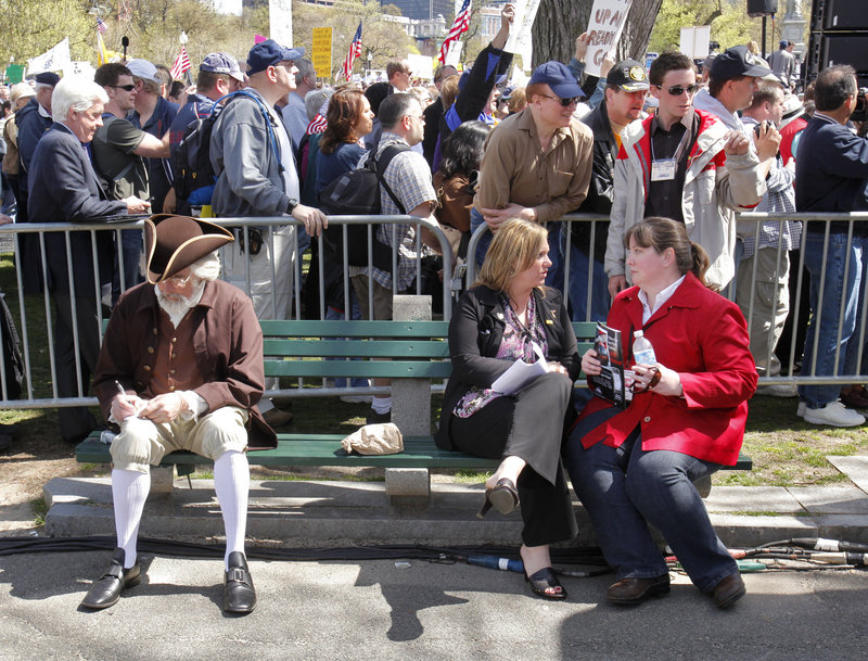 A costumed Jeff Cucci, left, of Albion writes on cards on a bench at Wednesday’s tea party rally in Boston. Cucci portrays Jacob Broom, a signer of the Constitution.
