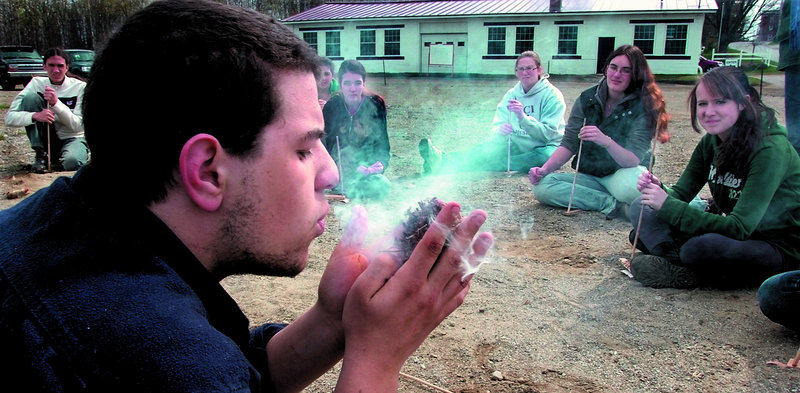 Unity College student Anthony Pono blows on smoldering wood shavings in a fire-starting demonstration.