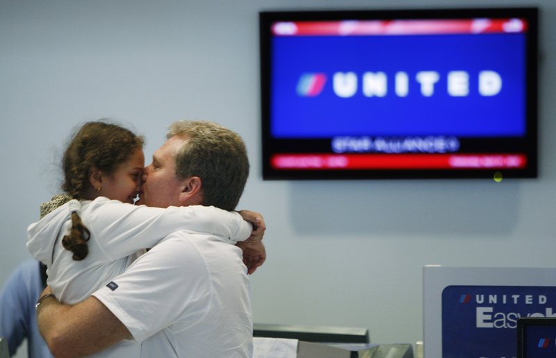 Andrey Zherikov kisses his daughter, Viktoria Zherikova, 7, as they wait at the United Airlines counter at Miami International Airport on Wednesday to find out if they can get a flight back home to Russia.