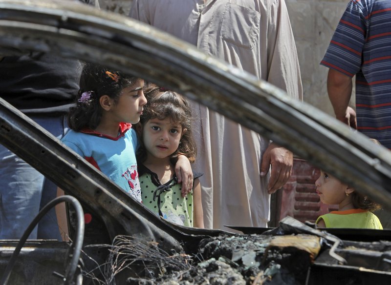 Zahra Naaim, 4, center, and Balqes Youssif, 6, left, stand next to a destroyed vehicle in the Shiite stronghold of Sadr City in Baghdad, Iraq, on Saturday, a day after bombings killed 69.