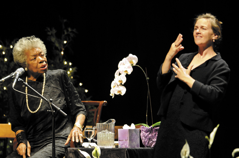 Maya Angelou, left, greets the crowd at the Augusta Civic Center with a song Monday. At right is sign language translator Margaret Haberman. The University of Maine at Augusta sponsored the poet's visit.