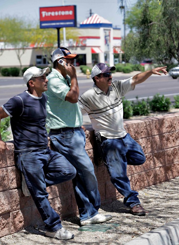 Jose Armenta, center, a 33-year-old illegal immigrant from Los Mochis, Sinaloa, Mexico, stands with his friend Vicente, left, while Julio Loyola Diaz of Juarez, Chihuahua, Mexico signals to motorists Wednesday in Phoenix. In the last two years, it is estimated that Arizona’s illegal population has decreased by about 100,000, down to about 460,000.