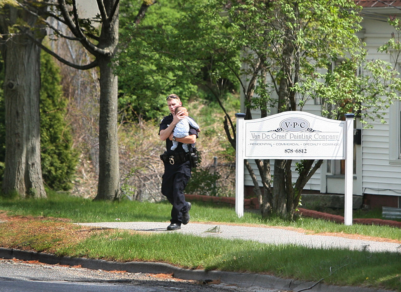 Eric Nevins, a Portland Police Department negotiator, carries a 5-month-old baby from an apartment during a police standoff on outer Forest Avenue in Portland on Sunday.