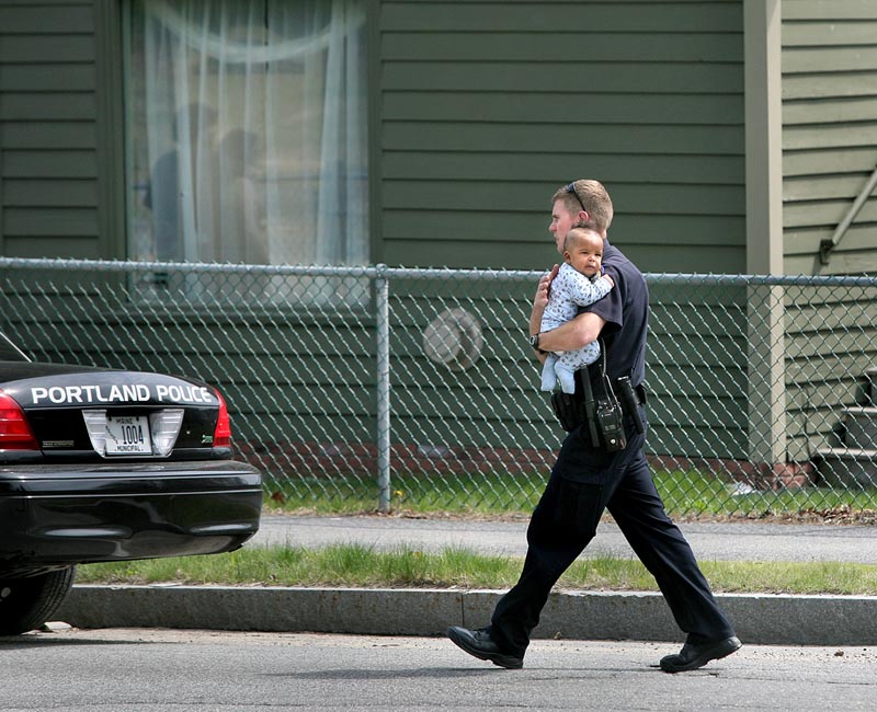 Portland Police Department negotiator Eric Nevins carries a 5-month-old baby to family members after the child was removed from an apartment during a police standoff on outer Forest Avenue on Sunday.