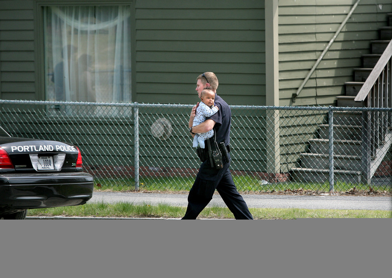 Eric Nevins, a Portland Police Department negotiator, carries a 5-month-old baby to family members after being removed from an apartment during a police standoff on outer Forest Avenue in Portland on Sunday.
