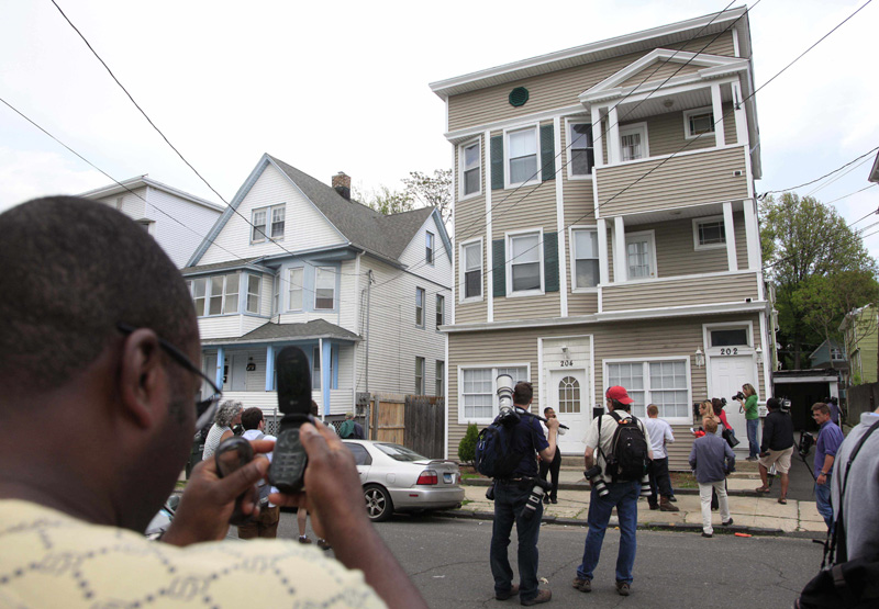 A local resident, left, and members of the media photograph a house in Bridgeport, Conn., today. Faisal Shahzad lived in the building's second floor apartment.