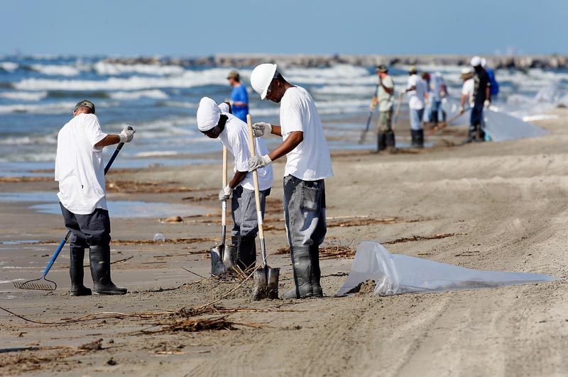 Workers collect oil and debris that washed up onto a beach in Grand Isle, La., Saturday. Oil from last month's Deepwater Horizon oil rig explosion in the Gulf of Mexico has started drifting ashore along the Louisiana coast.