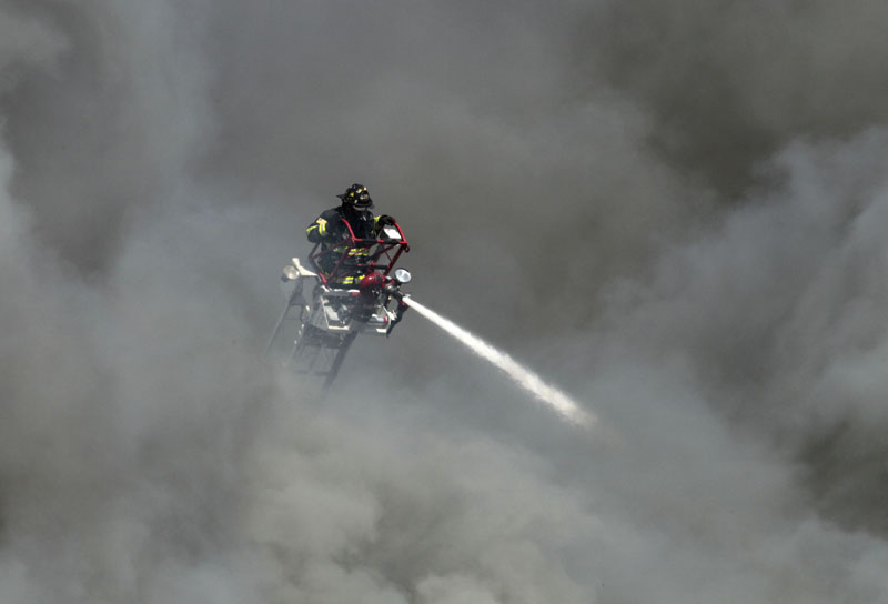 Thick, black smoke billows around a firefighter on a ladder as he pours water on a three-alarm fire at the former Jordan Meats building today. The plant was in the process of being demolished.