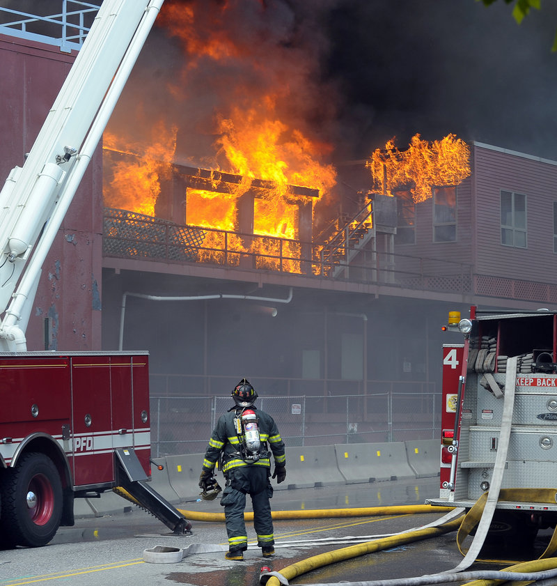 A Portland firefighter on Fore Street observes flames at the former Jordan’s Meats plant Thursday. The blaze is being investigated by Portland’s police and fire departments, the state Fire Marshal’s Office and the federal Bureau of Alcohol, Tobacco, Firearms and Explosives.