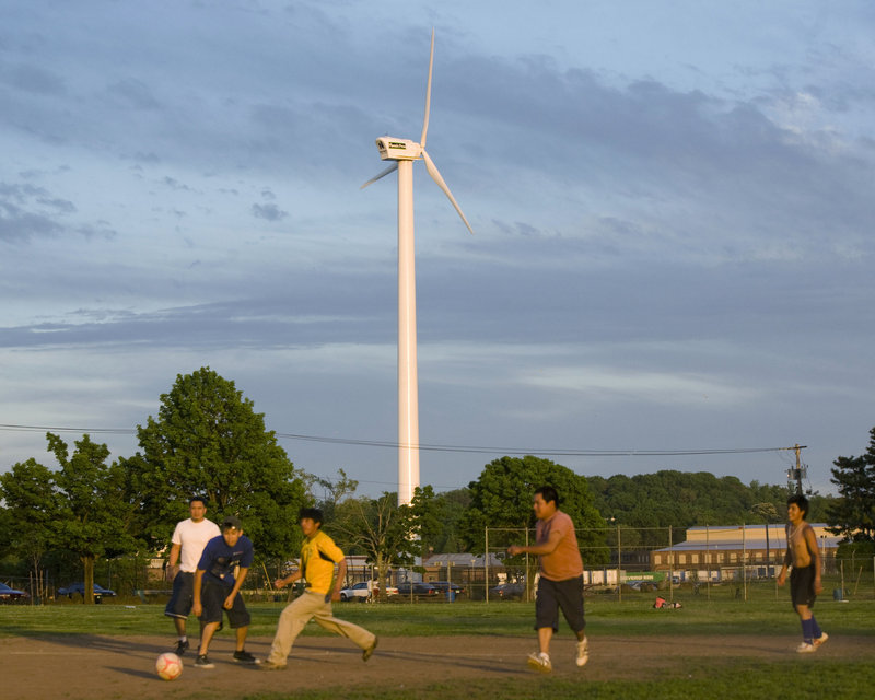 Soccer players take the field in Quinnipiac Park while a wind turbine spins on the grounds of Phoenix Press in New Haven, Conn., on Friday. In the drive for renewable energy, Connecticut is giving up on large-scale wind power, surrendering to poor topography and the limited reach of a shoreline that stops short of the Atlantic Ocean.