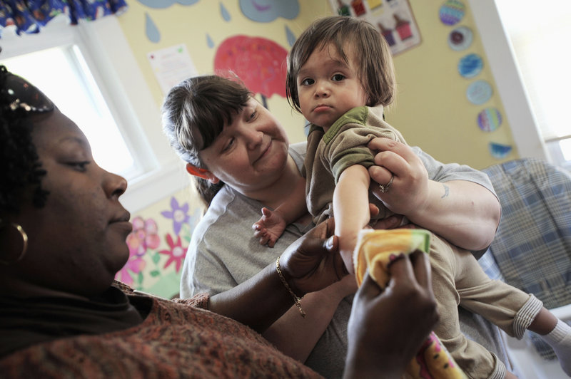 Mother House Crisis Nursery teacher Tammy Helton, rear, and family enhancement coordinator Tiltyla Stone clean pudding off 15-month-old Jesus at the facility in Rockford, Ill. Staff at the center worry that decreased funding will force the center to reduce its hours.
