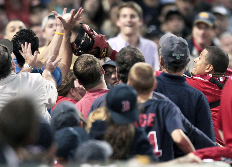 A fan grabs a foul ball above the glove of Boston catcher Victor Martinez, right, in the fourth inning Friday night at Fenway Park. It was that kind of night for the Red Sox, who surrendered 20 hits and 12 runs to the Royals.