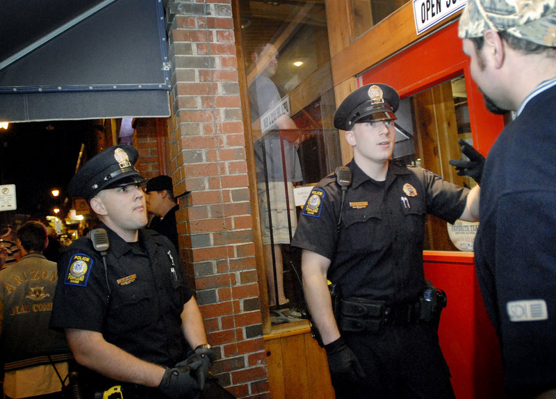 Portland Police Officers Evan Bomba, left, and Vincent Rozzi confer with a doorman at a Fore Street establishment in the Old Port on Friday night.