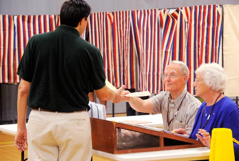 Cape Elizabeth voters cast their ballets at Cape Elizabeth High School on Tuesday morning. Assistant town clerks Scott Berry and Margaret Davenport hand a ballot to a Cape voter. (Photo by JohnEwing/ Staff photographer)