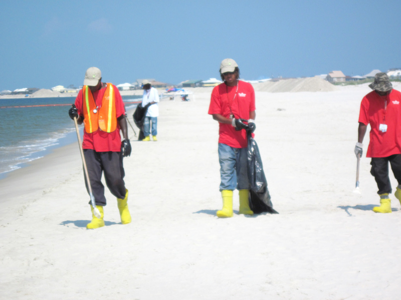 A cleanup crew patrols for oil Monday on a nearly deserted Dauphin Island beach. Out in the water, orange booms were positioned around the island to keep the oil from washing in.