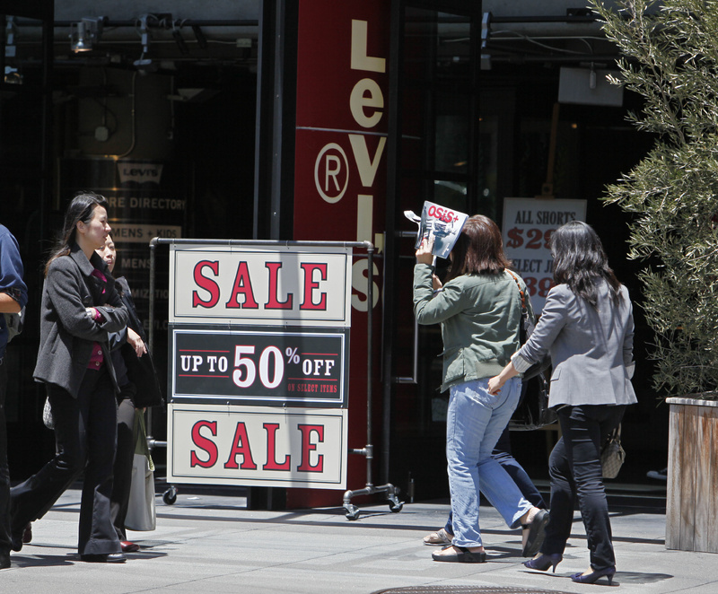 People walk by a sale sign at the entrance of the Levi’s store on Union Square in San Francisco. Retail sales plunged in May by the largest amount in eight months as consumers slashed spending on everything from cars to clothing.
