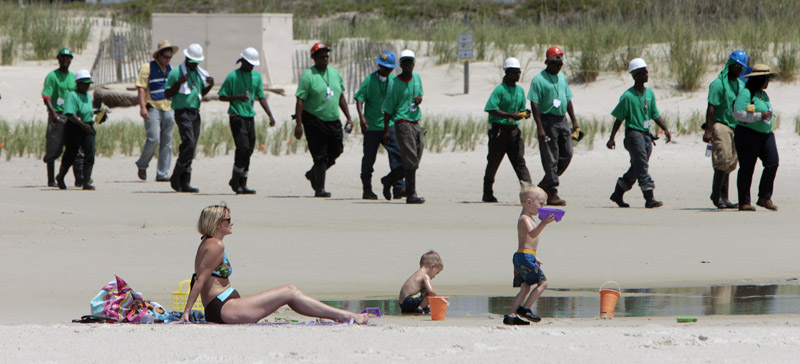 Mary Smith of Theodore, Ala., watches over her grandchildren as a large crew of cleanup workers walk along the beach in Dauphin Island, Ala. Oil from the Deepwater Horizon disaster has started washing ashore on the Alabama coast.