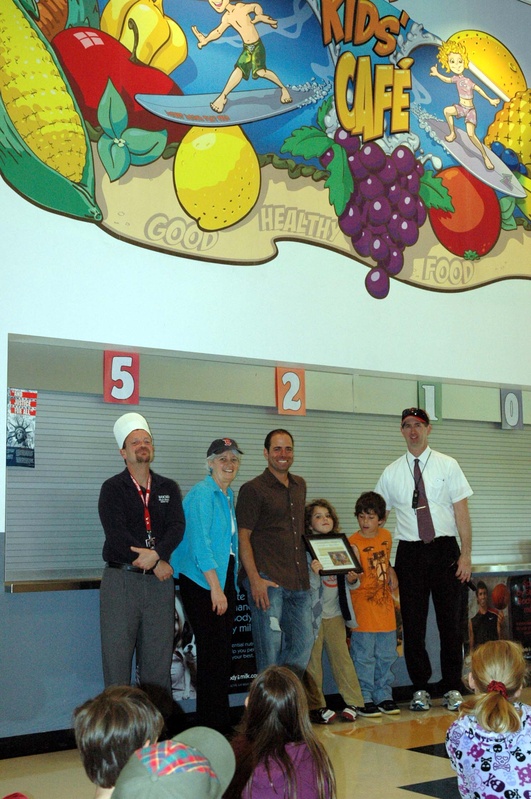 Wells-Ogunquit Community District Food Service Director Tyler Goodwin, Wells Elementary School Principal Marianne Horne, Wells resident Jason Talevi, Talevi’s daughter Olivia and son Jack and Assistant Superintendent Ken Spinney pose in front of a mural Talevi created and donated to the school in support of its nutrition promotion campaign.