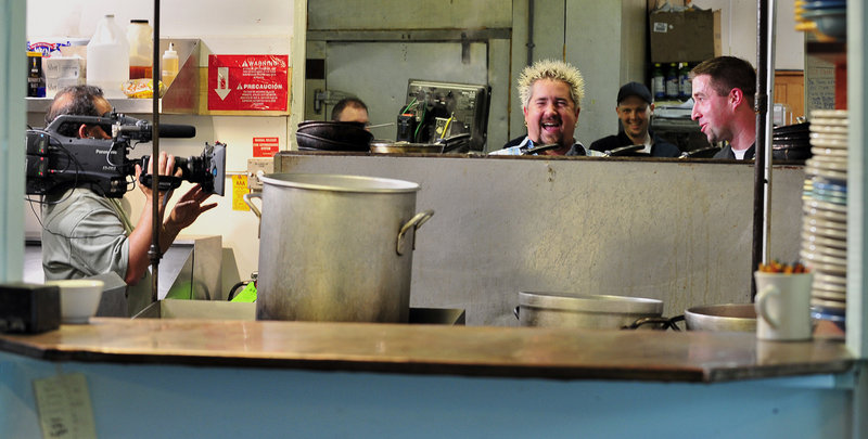 With cameras running, the cast and crew of the Food Network’s show, “Diners, Drive-ins and Dives” record at the Porthole Restaurant on the Custom House Wharf Tuesday. Guy Fieri, center, the show’s host, shares a laugh with chef Paul Dyer about his techniques for preparing fresh lobster for lobster rolls.
