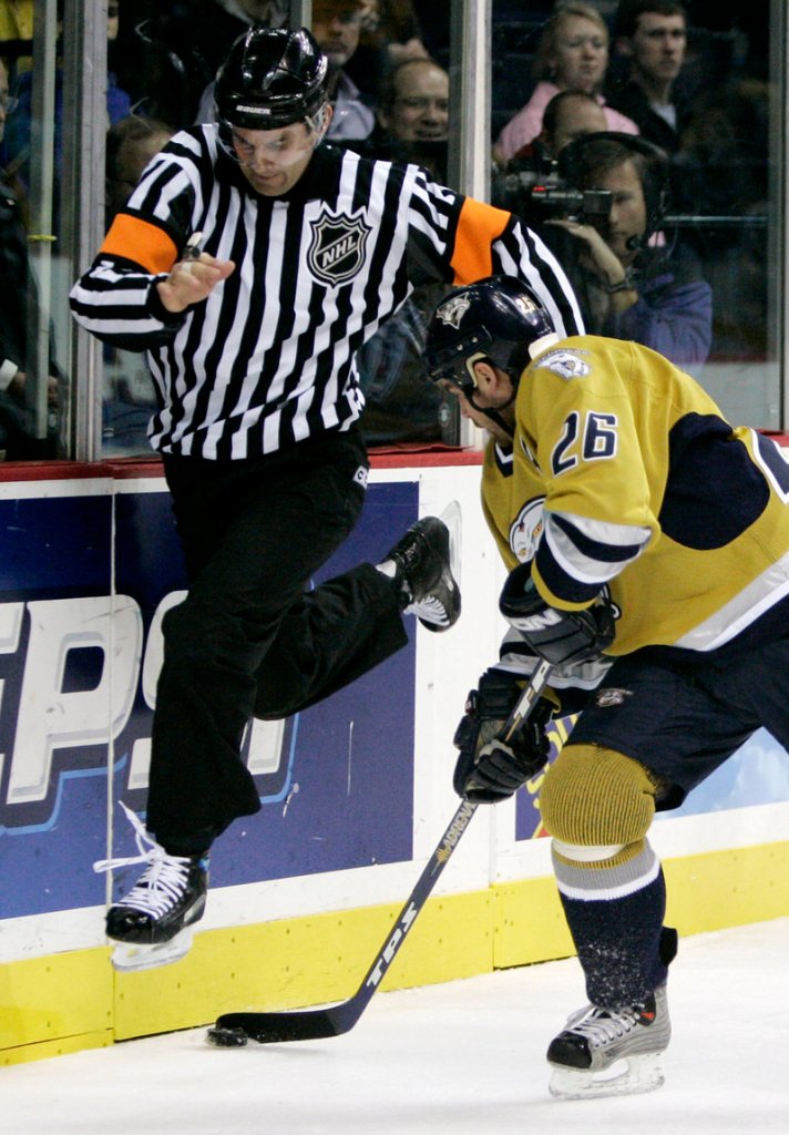 Referee Wes McCauley jumps over the puck as Nashville Predators right wing Steve Sullivan (26) digs it out against the boards.