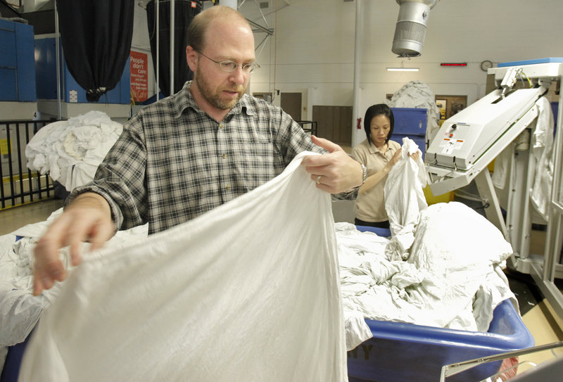 Reporter Ray Routhier loads a sheet onto a machine that will press and fold it at Maine Medical Center's linen services facility in Westbrook.
