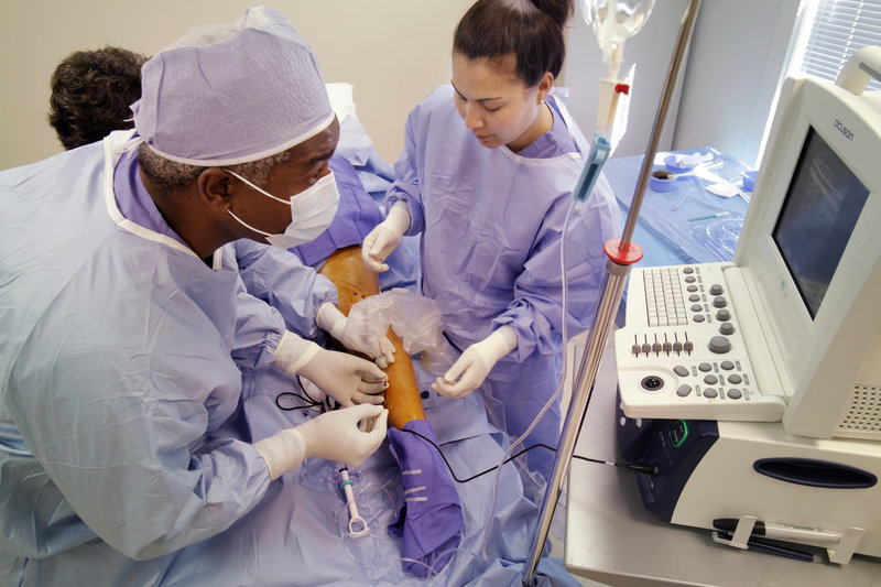 Dr. John Braxton inserts a closure catheter into a varicose vein in Laurette Poulin's right leg during a closure procedure last week. The procedure leaves the veins in place but seals them off so they no longer contain blood and quickly shrink. At right is Genevieve Allen, a medical assistant.